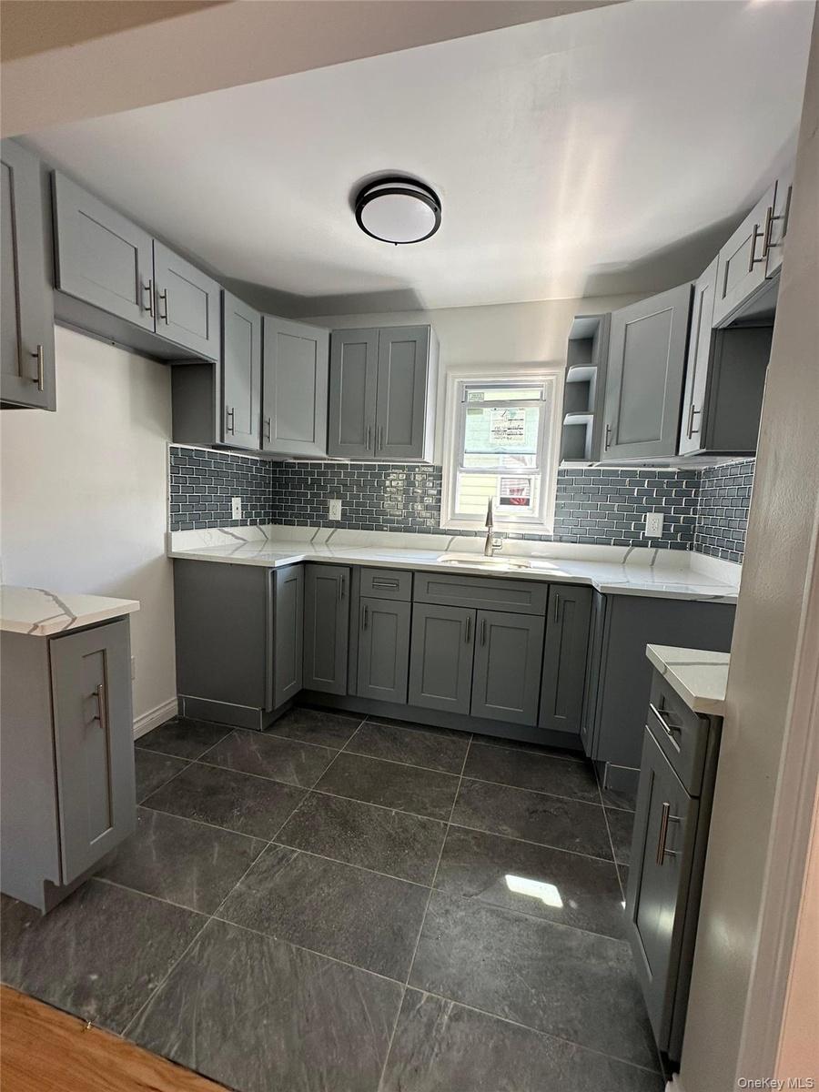 Kitchen featuring gray cabinetry, white countertops, a mosaic tile backsplash, stainless steel sink, and dark tile flooring