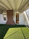 Covered porch with artificial turf flooring, featuring a red brick chimney, light gray siding, and white railing
