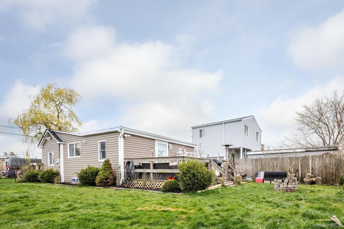 Rear exterior featuring beige horizontal siding, white trim, a gabled roofline, and a wood deck with lattice skirting