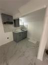 Kitchenette featuring gray shaker-style cabinetry, a built-in sink with a gooseneck faucet, a light-toned countertop, and an iridescent mosaic tile ba