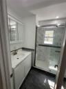 Bathroom featuring a white vanity with integrated sink, brushed nickel faucet, mirrored medicine cabinet, glass-enclosed shower, and dark tile floorin