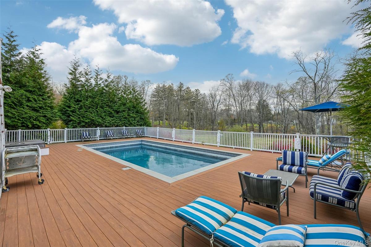 Expansive outdoor deck featuring an in-ground swimming pool, white picket fencing, and mature perimeter trees
