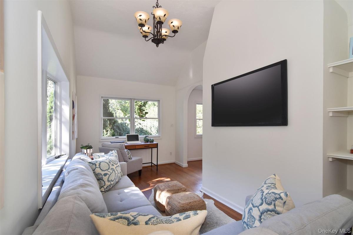Living area with wood finished floors, arched walkways, a desk, high vaulted ceiling, and a chandelier