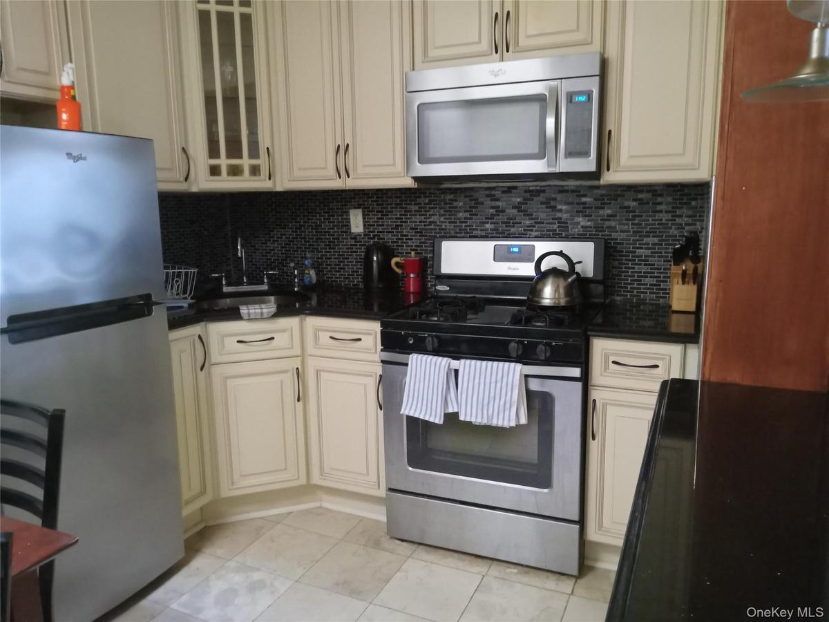 Kitchen featuring stainless steel appliances, black countertops, and a mosaic tile backsplash