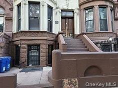 Brownstone facade featuring a prominent bay window, stone detailing, and a grand stoop entrance
