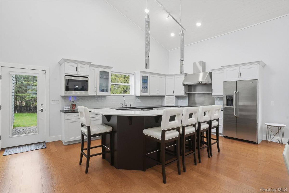 Vaulted ceiling kitchen featuring an expansive central island with seating, stainless steel appliances, white cabinetry, and wood-finish flooring