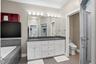 Bathroom featuring a dual-sink vanity with white cabinetry and dark countertop, large wall-mounted mirror, recessed bathtub with gray tile surround an