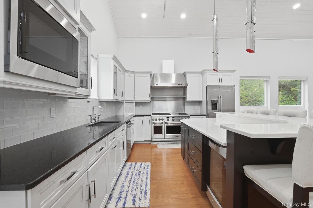 High-ceiling kitchen featuring white cabinetry, stainless steel appliances, dark countertops, and a central island with integrated seating