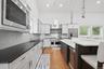 High-ceiling kitchen featuring white cabinetry, stainless steel appliances, dark countertops, and a central island with integrated seating