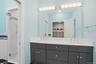 Bathroom featuring a double vanity with dark cabinetry and a light-toned countertop, dual sinks with chrome fixtures, and a large wall-mounted mirror