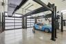 Spacious garage featuring light concrete flooring, multiple overhead garage doors with frosted panels, and two black metal car lifts