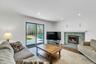 Living area featuring a stone-clad fireplace with a white mantel, recessed lighting, wood-finish flooring, a glass sliding door, and crown molding