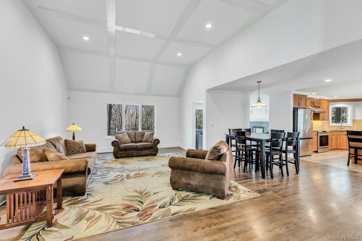 Open-concept living area featuring vaulted ceilings with beam detailing, hardwood flooring, and abundant natural light from multiple windows