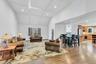 Open-concept living area featuring vaulted ceilings with beam detailing, hardwood flooring, and abundant natural light from multiple windows