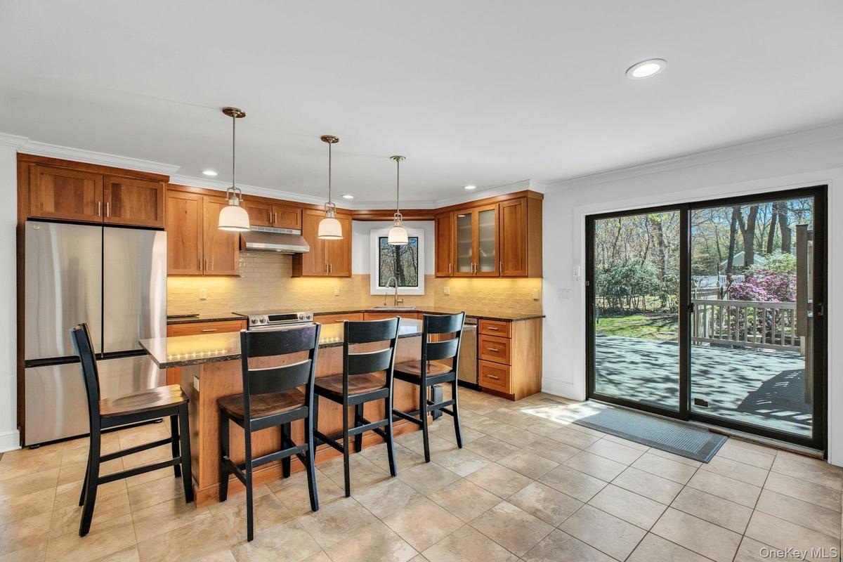 Kitchen featuring wood cabinetry, stainless steel appliances, a center island with pendant lighting, tile flooring, and sliding glass doors opening to