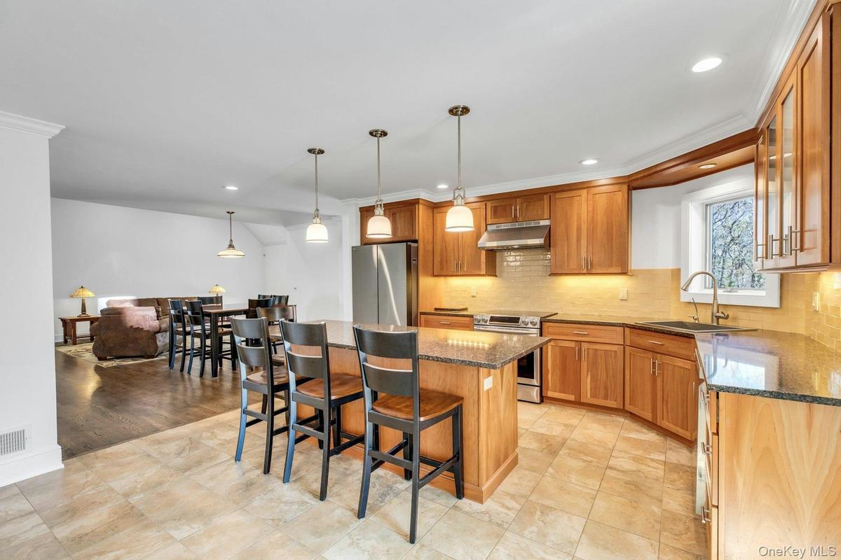 Spacious kitchen featuring warm wood cabinetry, granite countertops, stainless steel appliances, and tile flooring