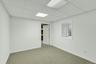 Carpeted room featuring crisp white walls, a drop ceiling with integrated lighting, a white painted door frame, and a window with horizontal blinds