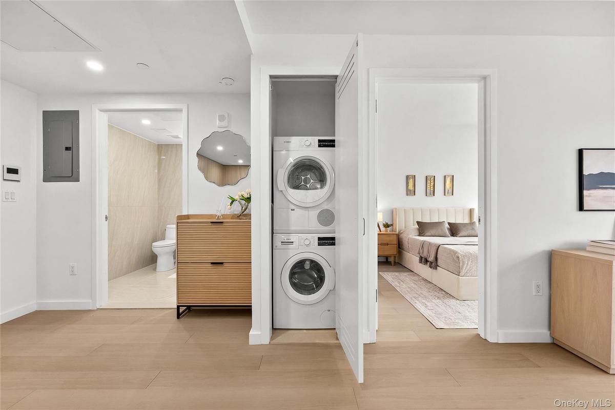 Laundry area featuring electric panel, stacked washer and clothes dryer, light wood-type flooring, and recessed lighting