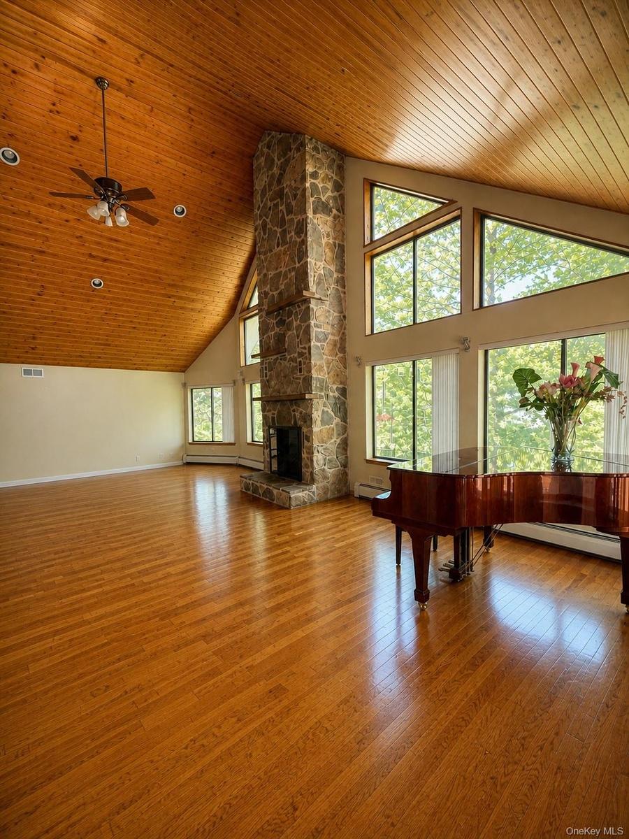 Spacious room featuring wood-finish flooring, a vaulted wood-paneled ceiling, a stone fireplace, large windows, and recessed lighting
