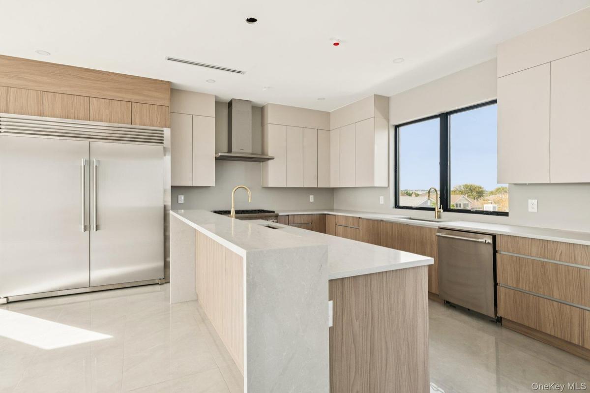 Kitchen with modern cabinets, appliances with stainless steel finishes, light stone counters, wall chimney range hood, and light tile patterned floori