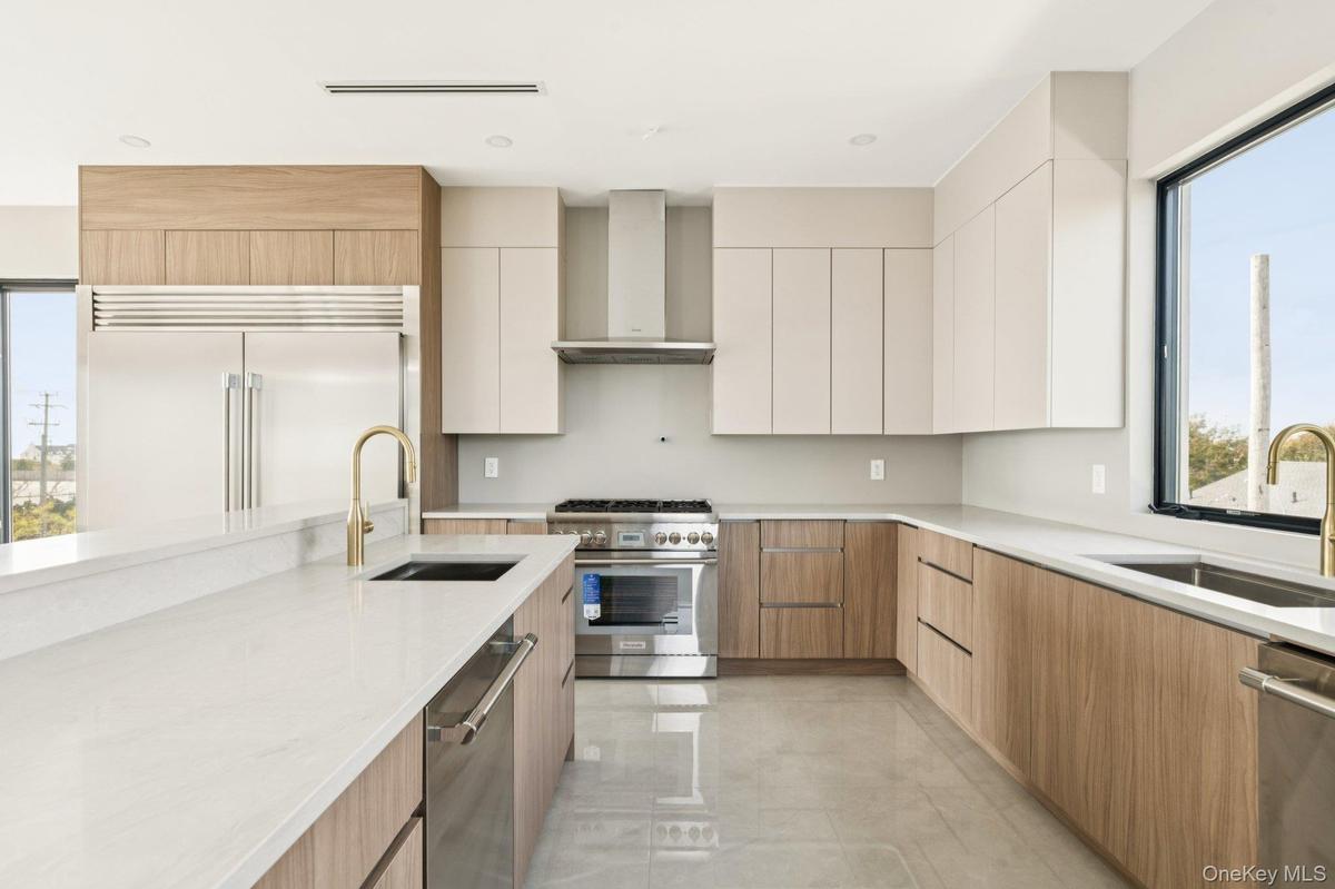 Kitchen featuring modern cabinets, high end appliances, light stone counters, wall chimney exhaust hood, and light tile patterned floors