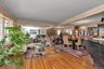 Hardwood flooring extends throughout this expansive living and dining area, featuring mirrored wall accents and a window with vertical blinds