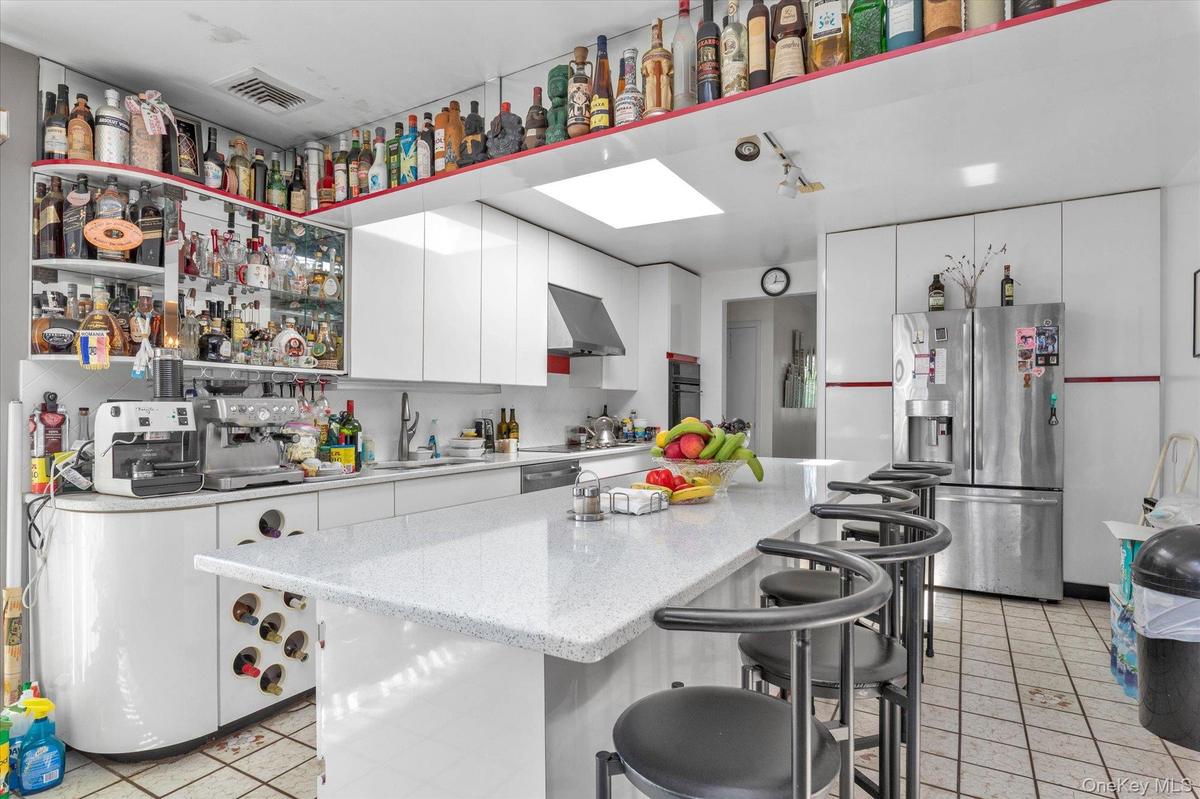 Open-concept kitchen featuring an expansive island with seating, white cabinetry, a built-in wine rack, and a skylight