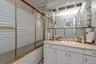 Bathroom vanity with an integrated sink, polished brass fixtures, and an expansive mirror featuring recessed lighting