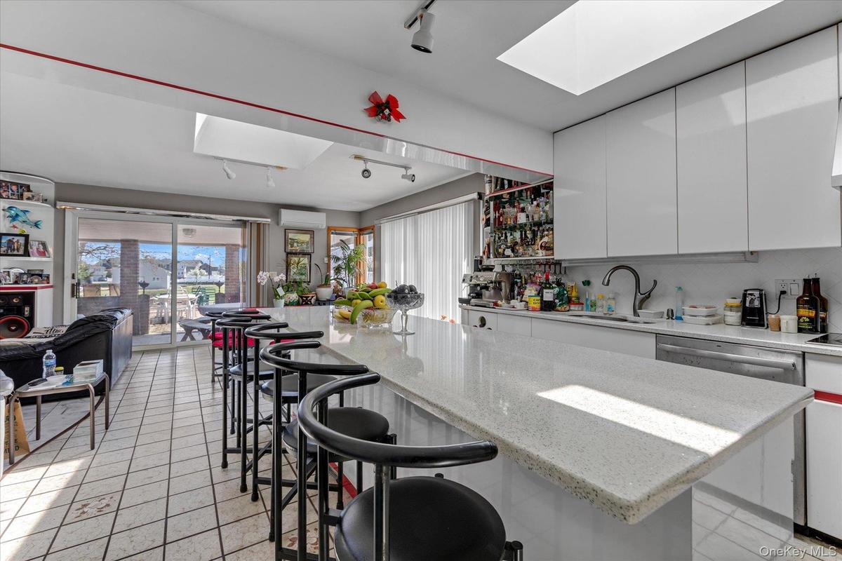 Kitchen featuring a spacious island with seating, white cabinetry, and a large skylight