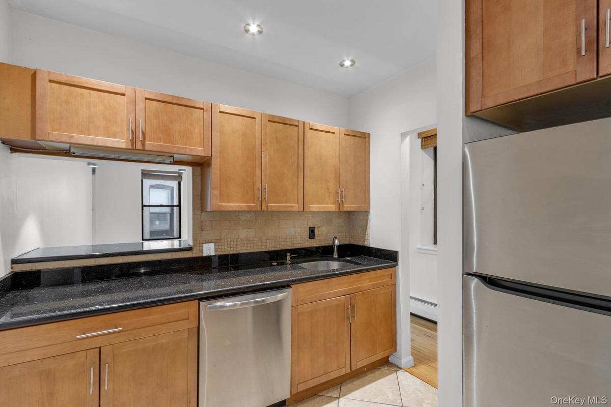 Kitchen featuring wood cabinetry, dark countertops, an undermount stainless steel sink, and a stainless steel dishwasher