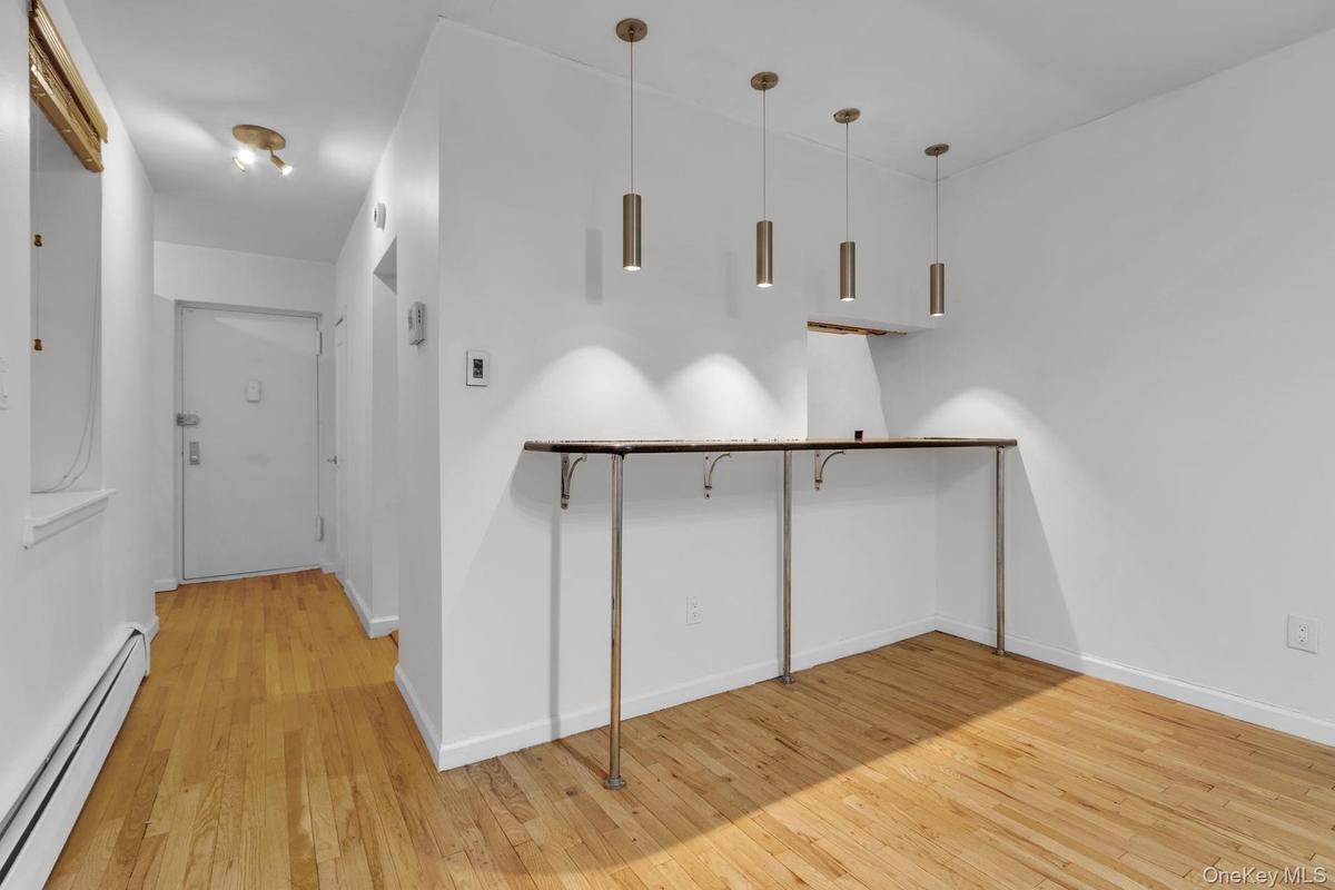 Hardwood flooring extends throughout this space, complemented by a built-in counter with metallic supports and three pendant light fixtures