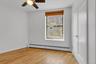 Room featuring wood-finish flooring, white walls, and a window with wood blinds