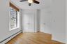 Wood-finish flooring paired with white walls, a window featuring horizontal blinds and security bars, a ceiling fan with integrated lighting, and two 