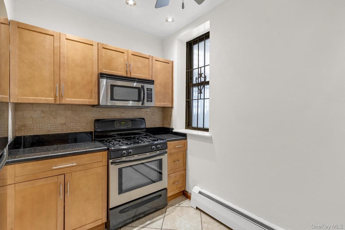 Kitchen featuring light wood cabinetry, black countertops, a stainless steel gas range, and an over-range microwave