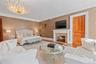 Spacious room featuring a prominent fireplace with a stone surround and white mantel, a large decorative chandelier, light wood-finish flooring, and a