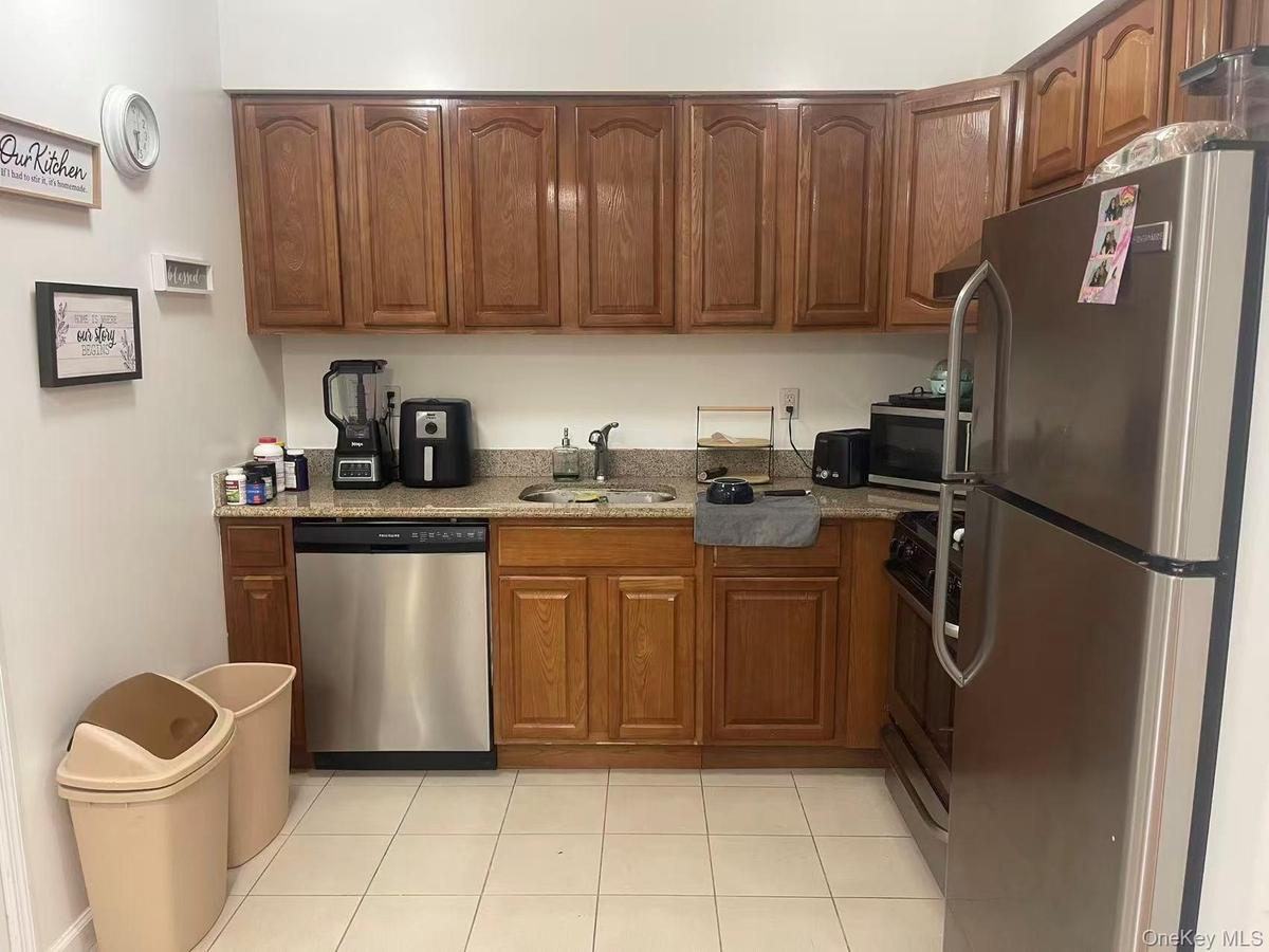 Kitchen featuring wood-finish cabinetry, granite-style countertops, stainless steel refrigerator, stainless steel dishwasher, and tile flooring