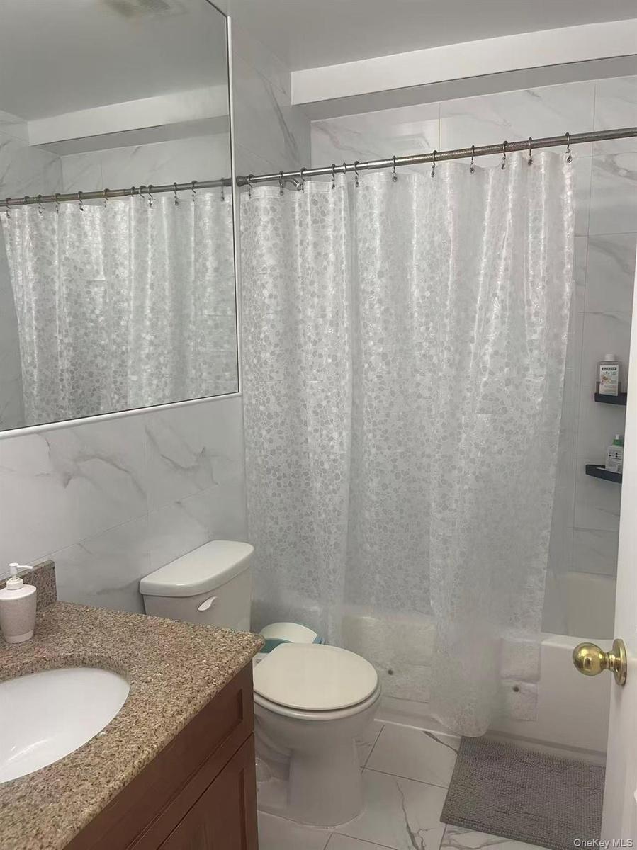 Bathroom featuring a built-in tub with a shower fixture, white ceramic toilet, and a vanity with a granite-look countertop and integral sink
