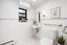 Well-lit bathroom featuring white tiled walls with a light green accent stripe, hexagonal floor tiles, a pedestal sink with exposed plumbing, a toilet