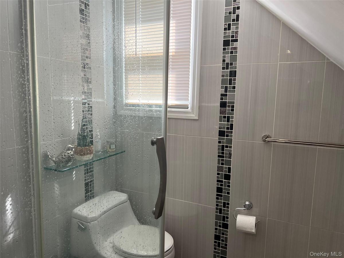 Shower enclosure featuring glass door, tiled walls with decorative mosaic accent, and integrated glass shelving