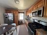 Galley kitchen featuring light wood cabinetry with crown molding, stainless steel appliances, speckled stone countertops, and a mosaic tile backsplash