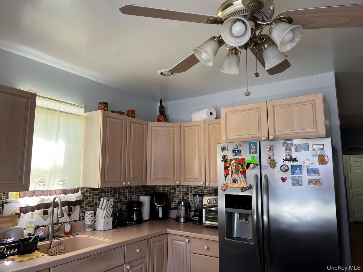 Kitchen featuring light wood-finish cabinetry, a built-in stainless steel refrigerator, and a mosaic tile backsplash