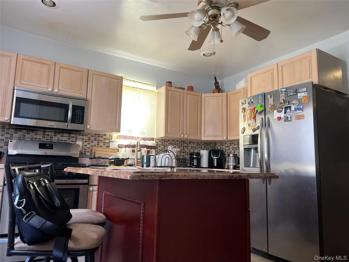 Kitchen featuring light-toned cabinetry, stainless steel appliances, a mosaic tile backsplash, and a central island with a wood-finish base and speckl