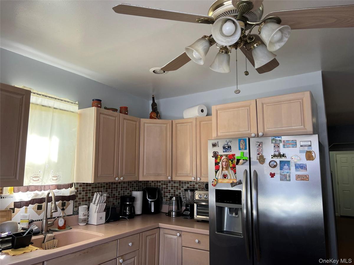 Kitchen featuring light wood-finish cabinetry, a patterned tile backsplash, and a stainless steel side-by-side refrigerator
