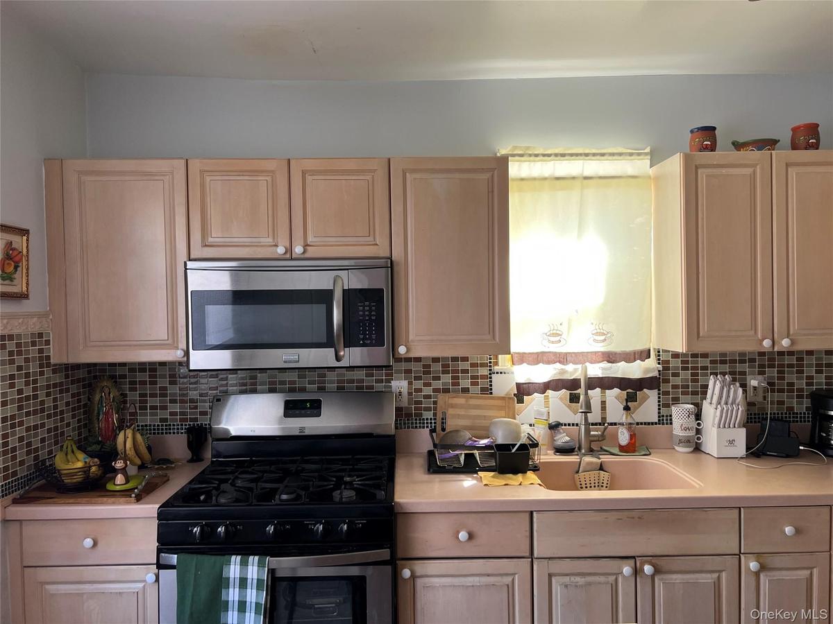 Kitchen featuring light wood-finish cabinetry, stainless steel microwave, stainless steel range, mosaic tile backsplash, and light pink countertops
