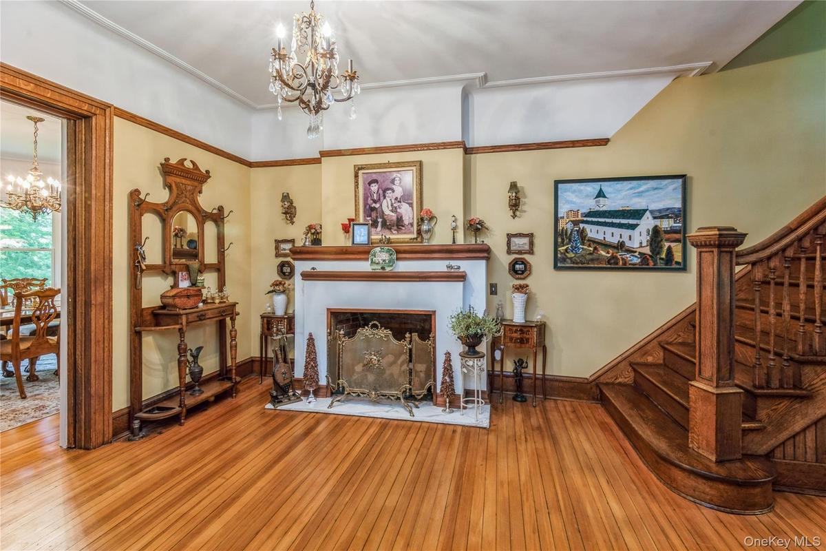 Spacious entry hall featuring wood-finish flooring, a decorative fireplace with a mantel, a chandelier, and an intricately carved wooden staircase