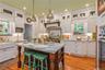Gourmet kitchen featuring a central island with granite countertop, white shaker cabinetry with brass hardware, subway tile backsplash, and wood-finis