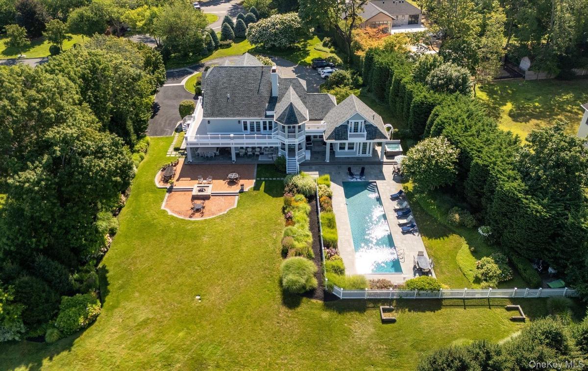 Expansive backyard featuring a rectangular swimming pool, a substantial paver patio with a built-in fire pit, and a spacious upper-level balcony