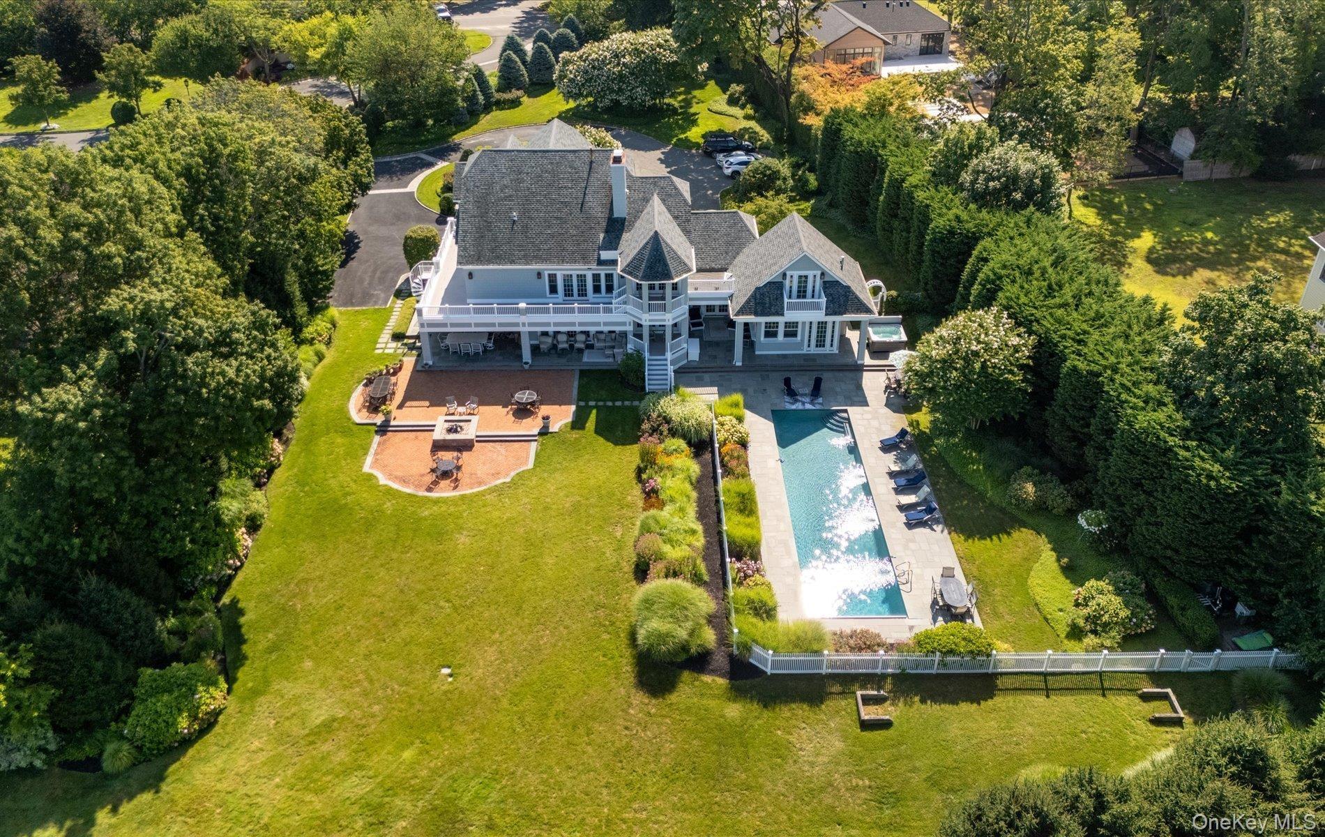 Expansive backyard featuring a rectangular swimming pool, a substantial paver patio with a built-in fire pit, and a spacious upper-level balcony