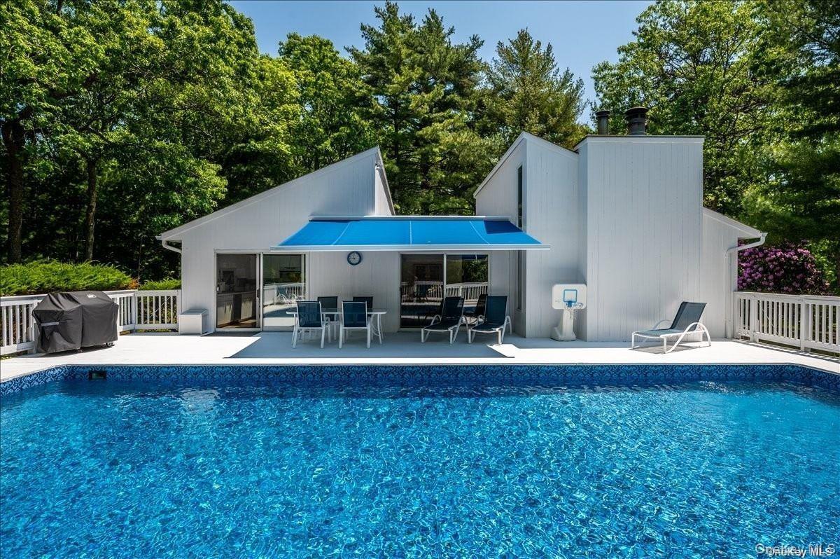 Outdoor swimming pool featuring a white deck surround, modern architecture with clean lines, a blue awning over the patio, and a large white deck with