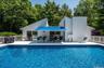Outdoor swimming pool featuring a white deck surround, modern architecture with clean lines, a blue awning over the patio, and a large white deck with